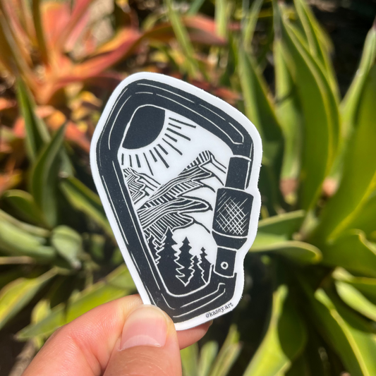 Black and white carabiner sticker with a design of a nature mountain scene against a green plant background