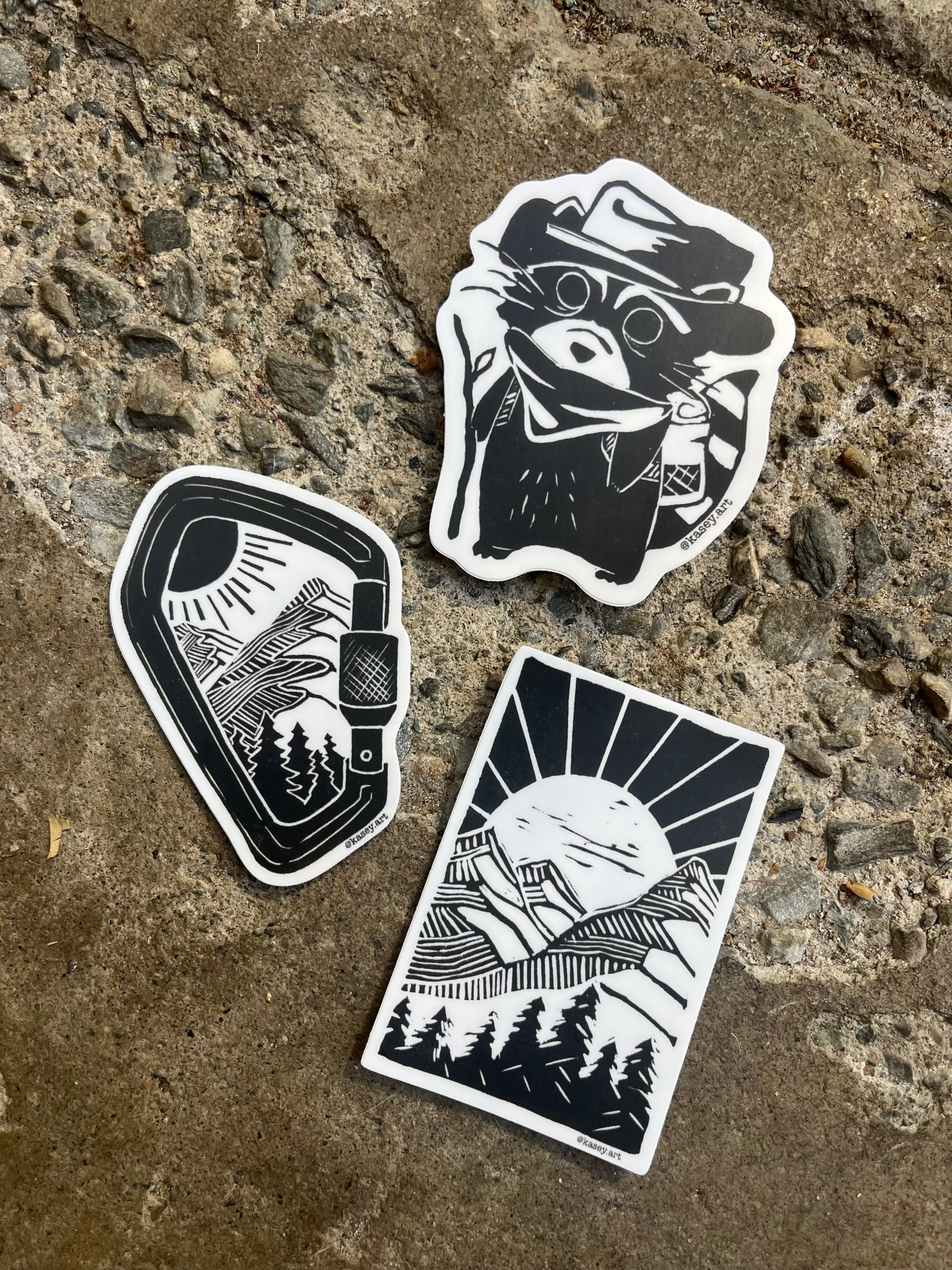 Three black and white nature themed stickers on a textured stone surface